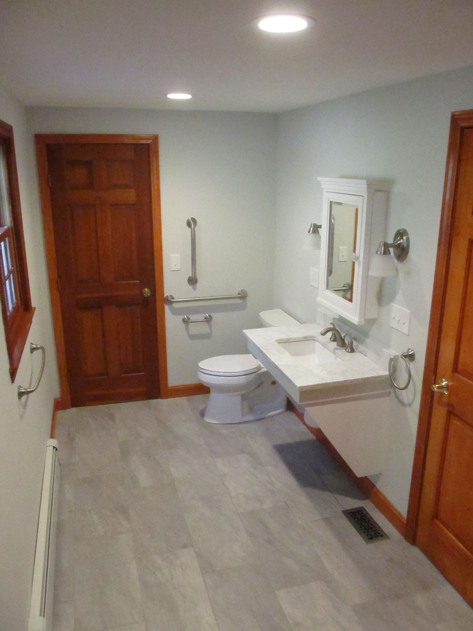 Accessible bathroom with toilet, wall-mounted sink, mirror, and wood doors on either side.