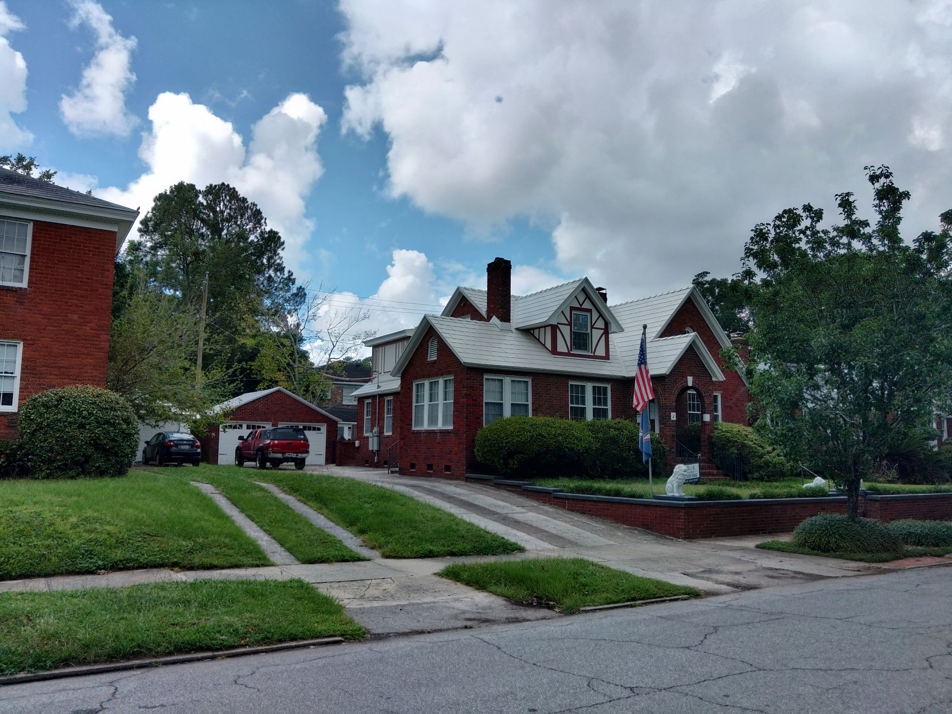 Brick house with white trim, driveway, and green lawn under a cloudy sky