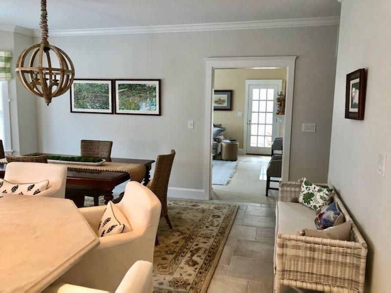 Bright dining room and hallway with beige furniture, rug, framed art, and wicker basket chair