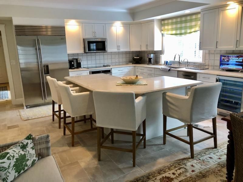 Bright white kitchen with a large island, bar stools, stainless fridge, and built-in microwave