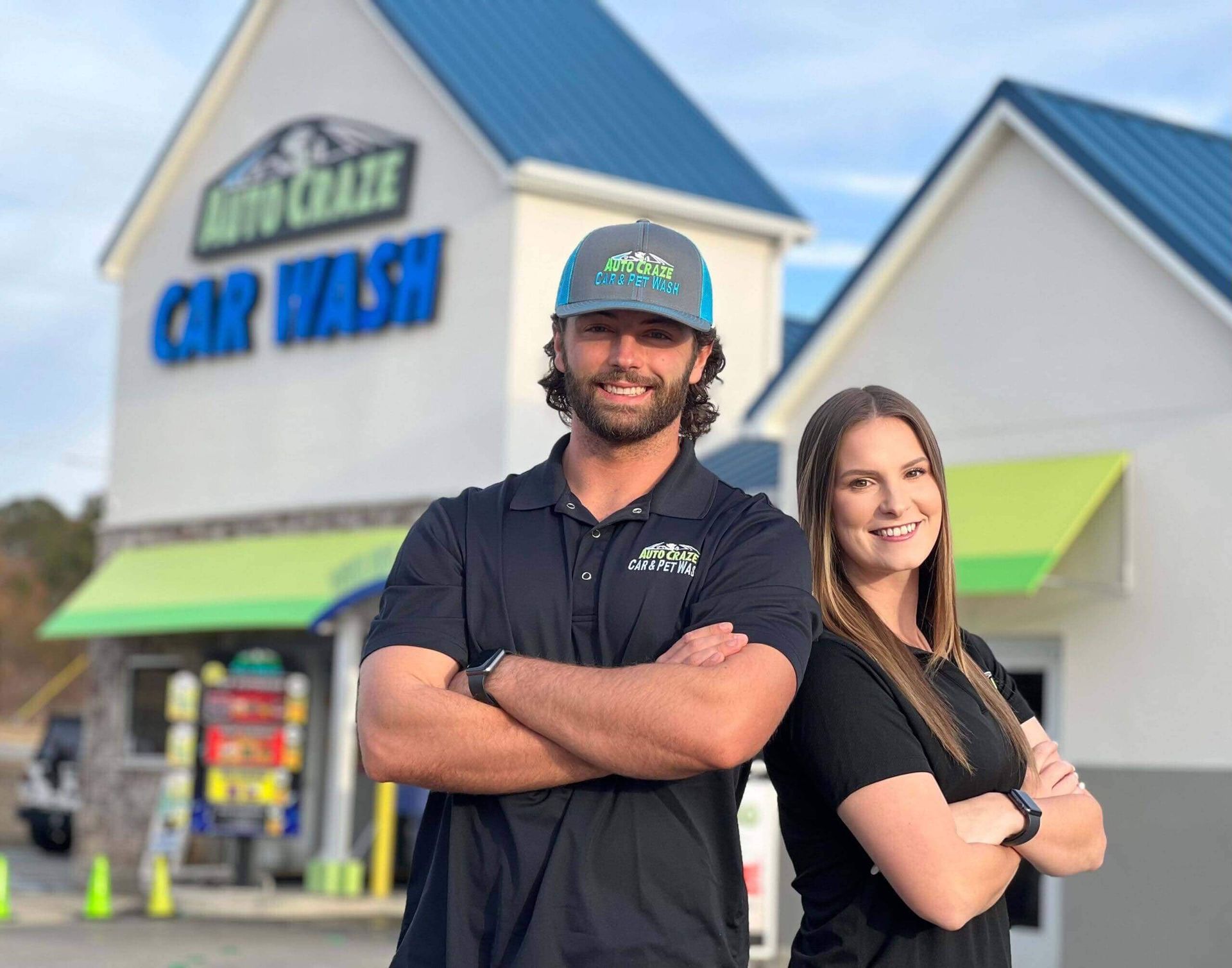Two people standing in front of Auto Craze Car Wash. Man in a hat has arms crossed. Woman has arms crossed.