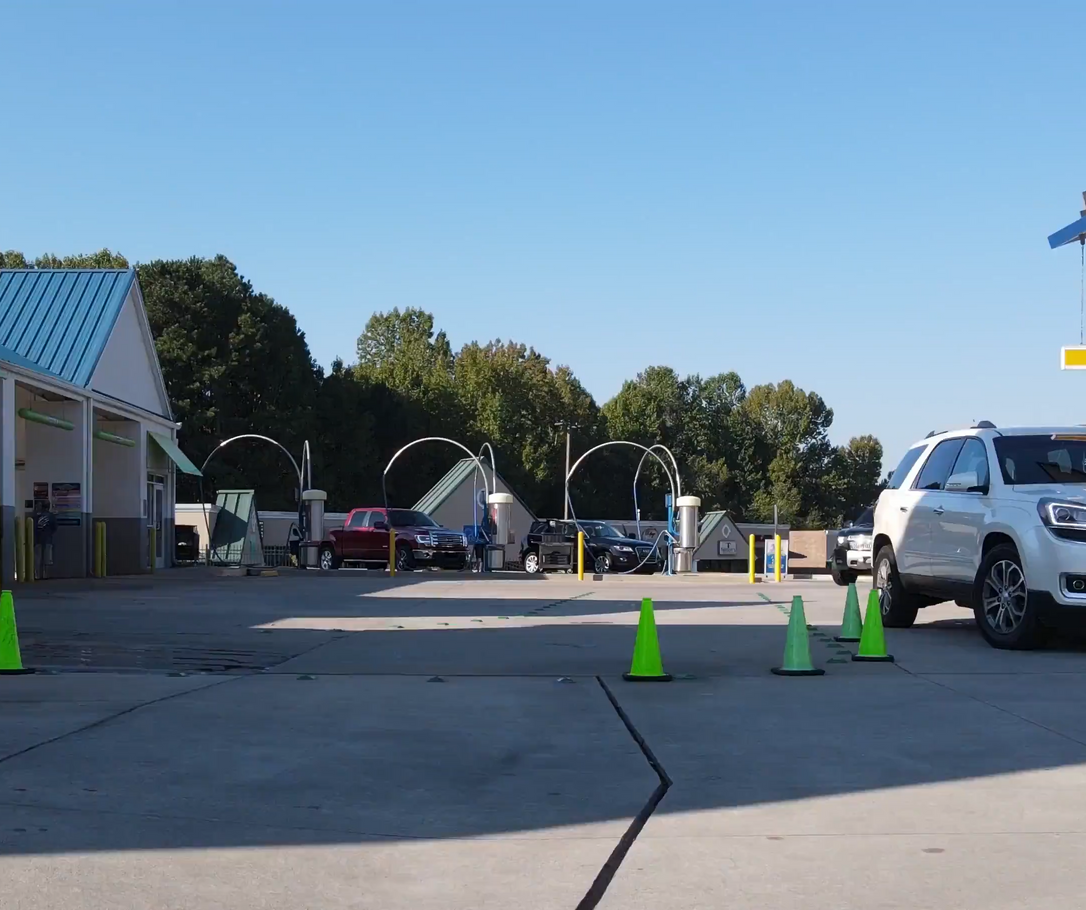 Car wash with several cars in line, under a blue sky. Green and yellow cones guide traffic.