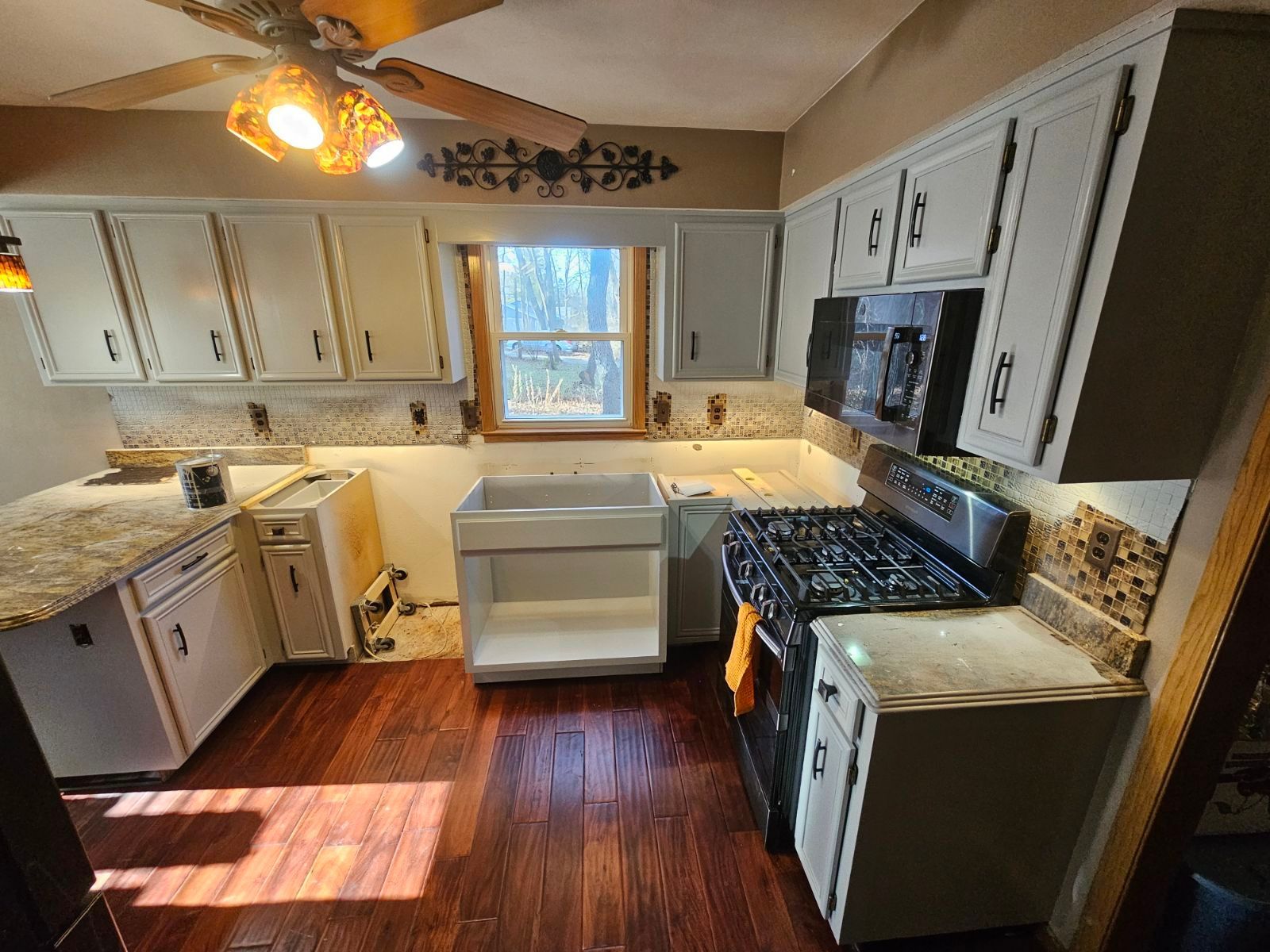 a kitchen with white cabinets , a stove , a sink , and a ceiling fan .