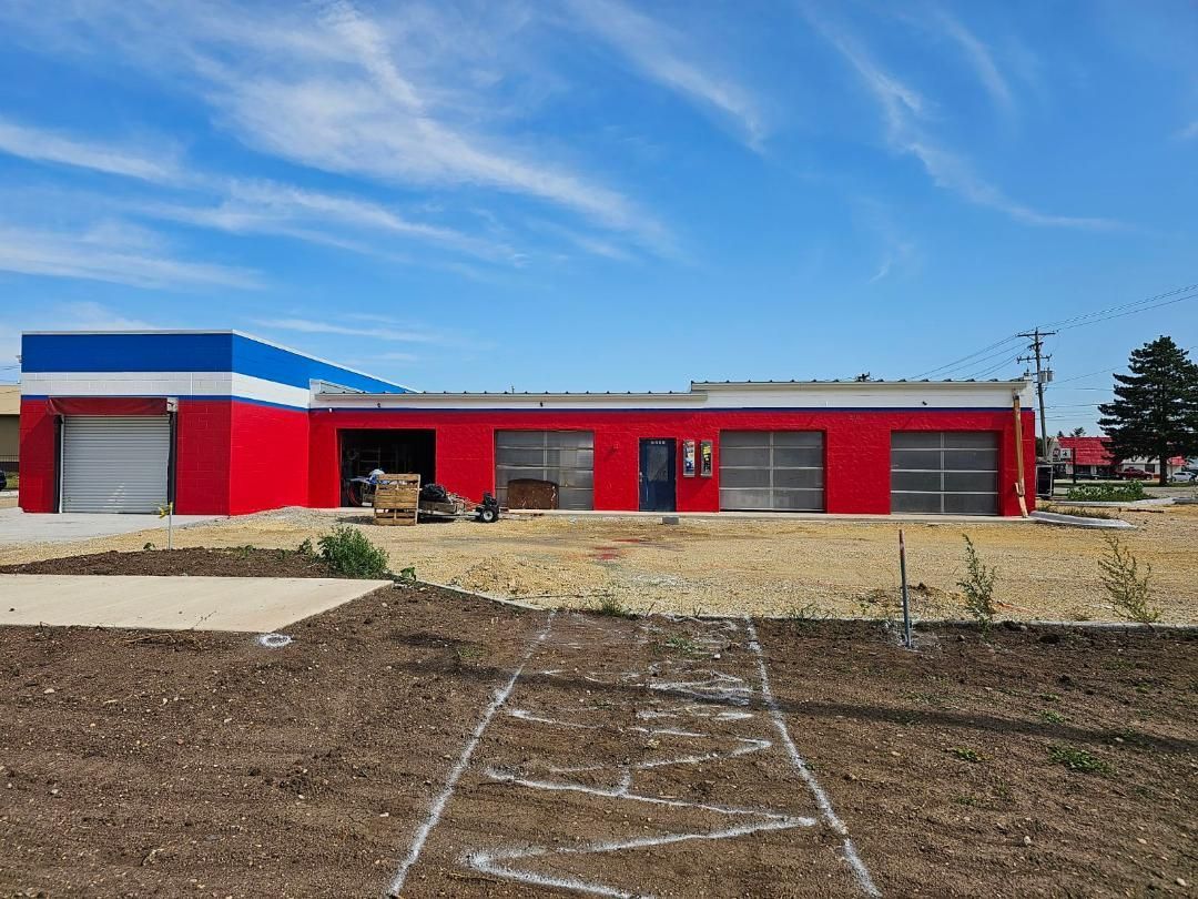 a red , white and blue building is sitting in the middle of a dirt field .