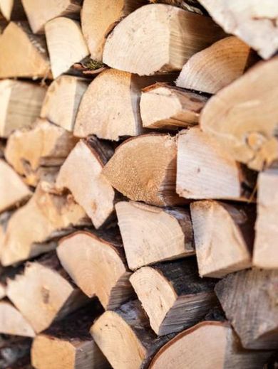 Pile of split firewood, beige and brown, stacked for drying.