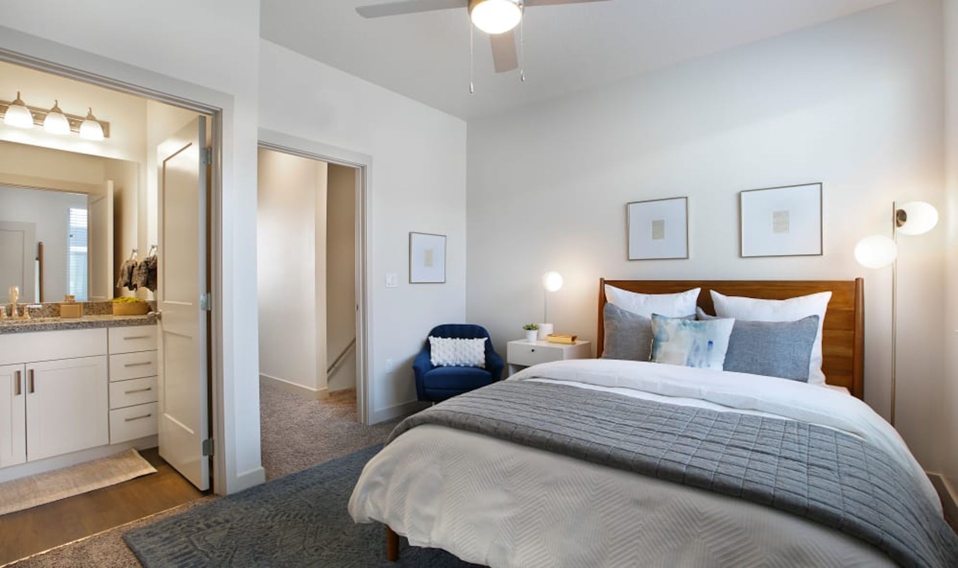 Bedroom with a bed, bathroom, and hallway. Light walls, blue and white accents, cozy.