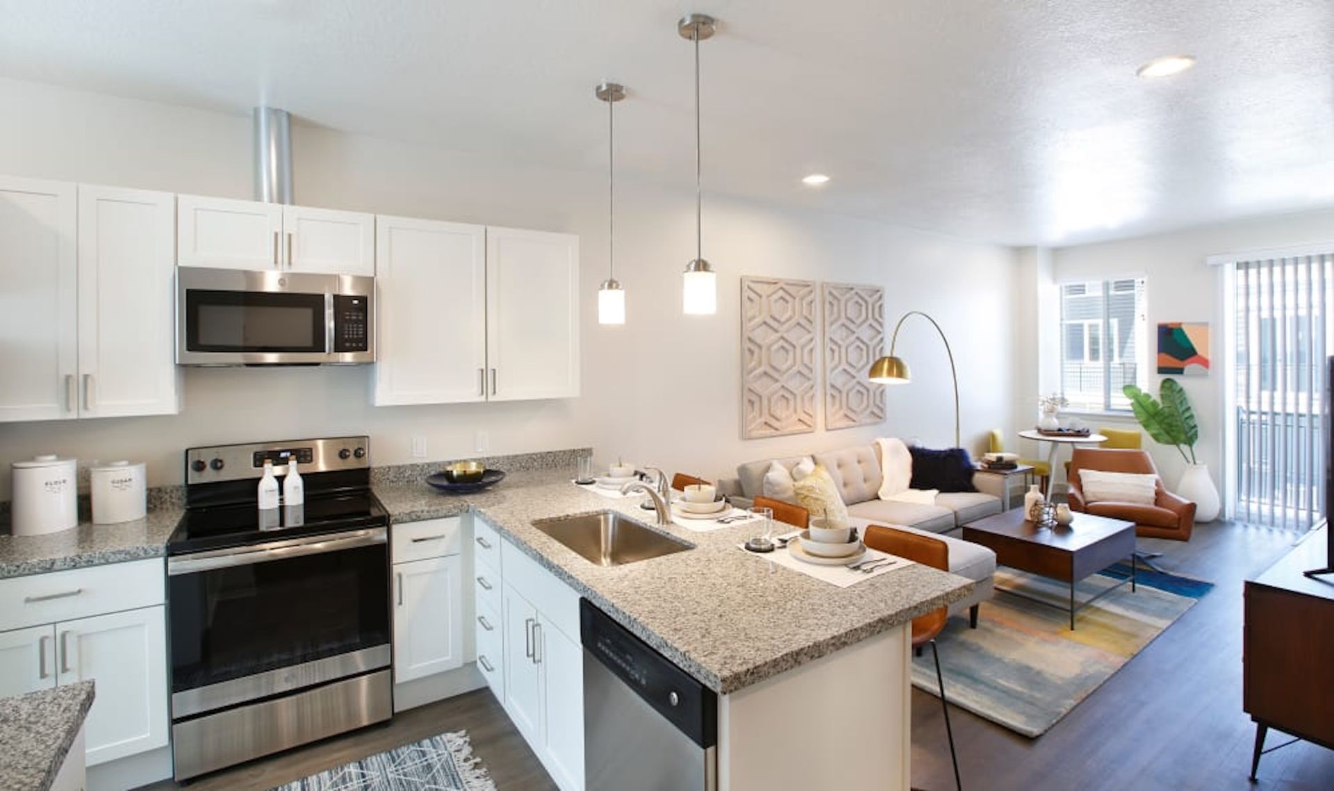 Modern apartment kitchen and living area with stainless steel appliances, granite counters, and a gray sofa.