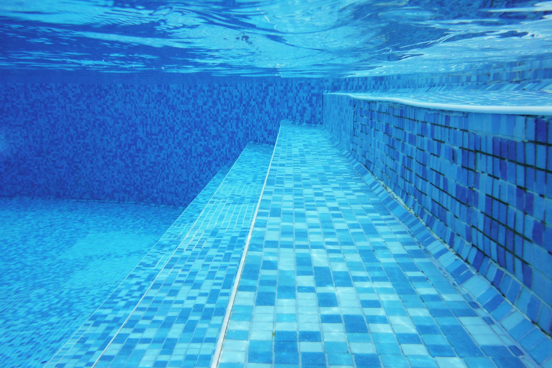 Underwater shot of blue stairs and tiles on a pool bottom.