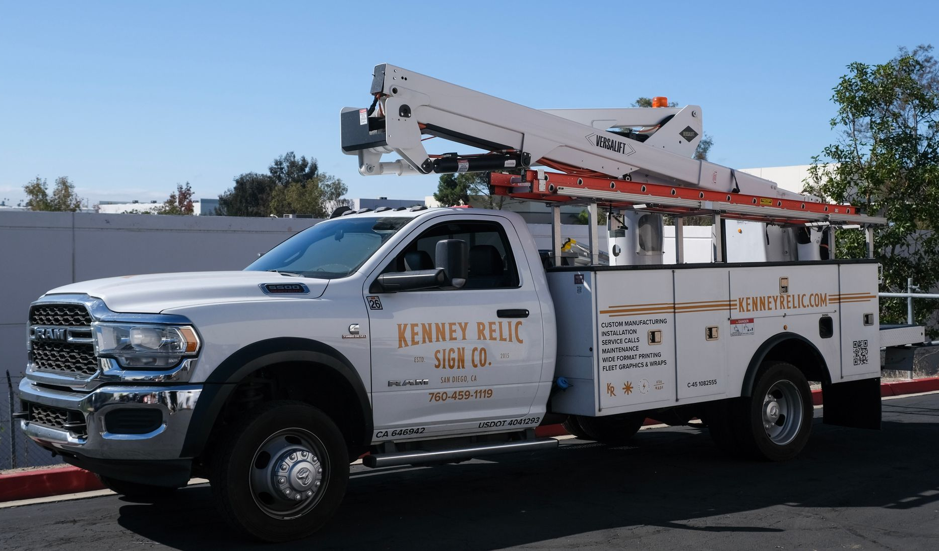 White utility truck with ladder racks and company branding parked outdoors in sunlight