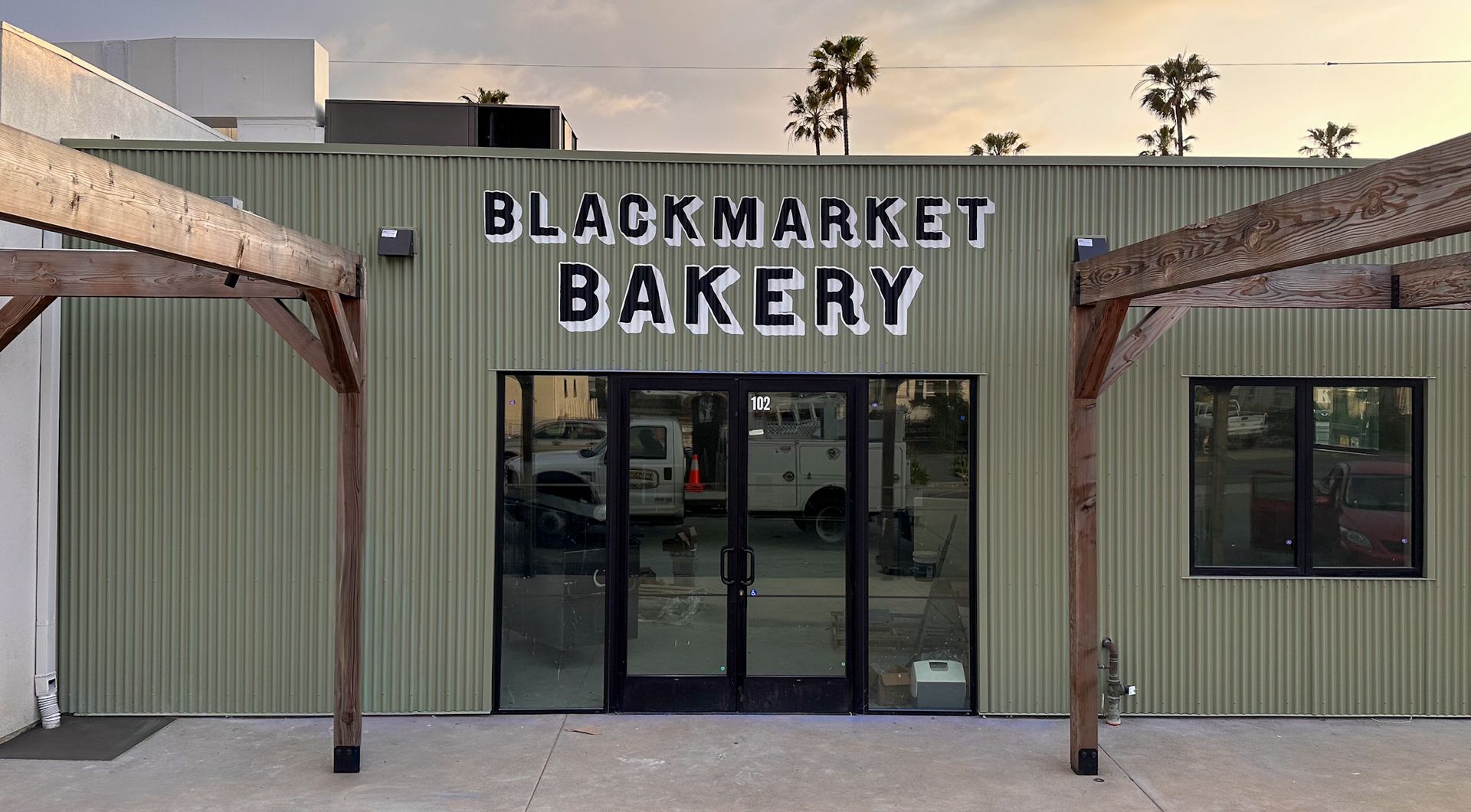Blackmarket Bakery storefront with green facade, large windows, and wooden pergola.