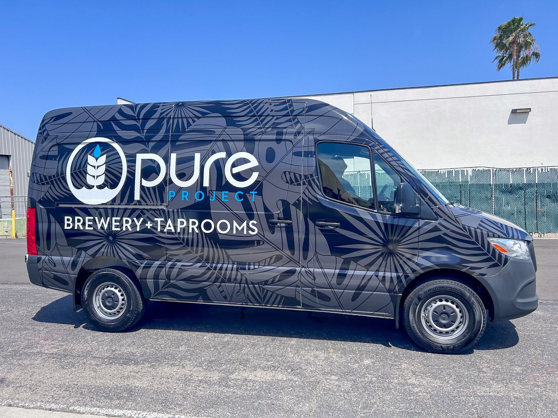 Van with Pure Project Brewery logo and tropical leaf pattern. Blue sky background.
