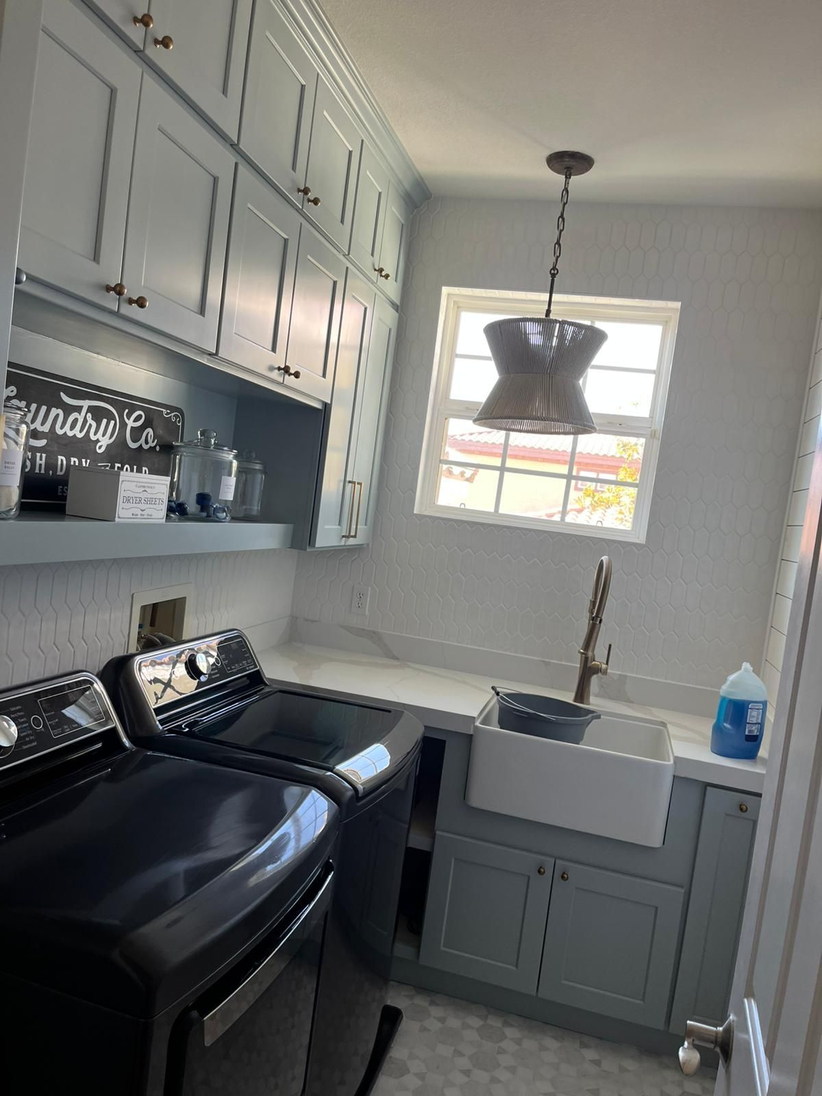 Laundry room with blue cabinets, black washer and dryer, and a sink by a window.