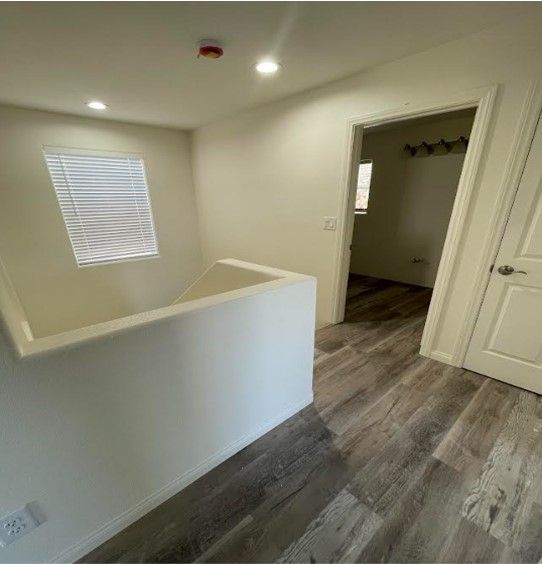 A hallway with a white railing, wood-look flooring, and a doorway leading to a room with a closet.