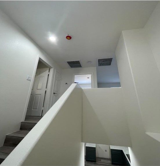 Interior view of a white staircase leading to a hallway with multiple doors and an open space at the top, lit by recessed ceiling lights.