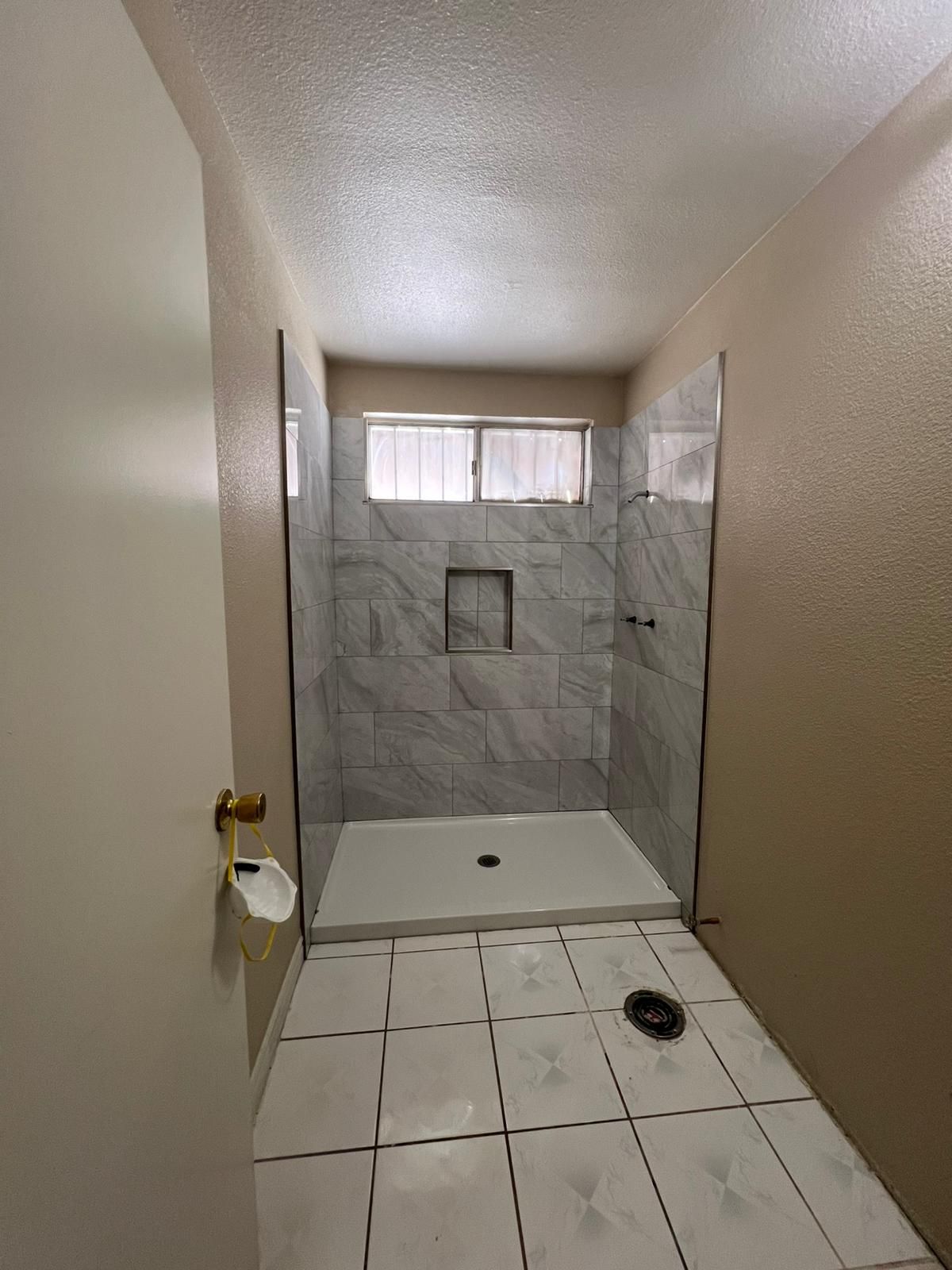 Newly renovated bathroom with a tiled shower stall and white floor tiles. The shower has a built-in niche and window.