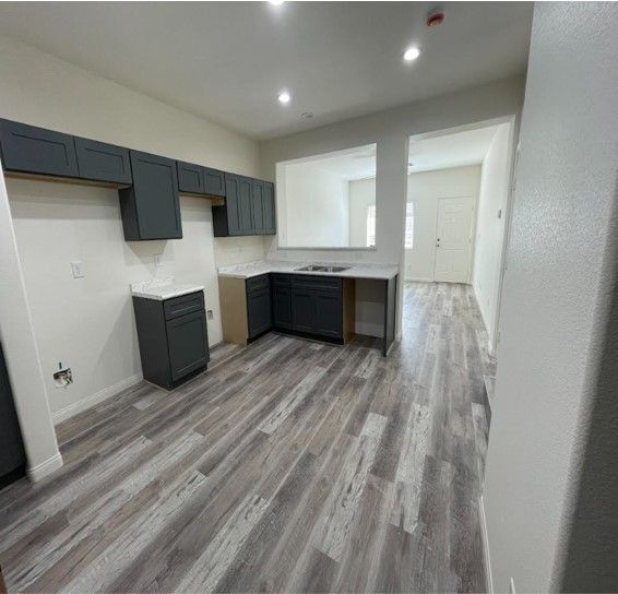 A modern kitchen with grey cabinets, wood-look flooring, and a pass-through to another room.