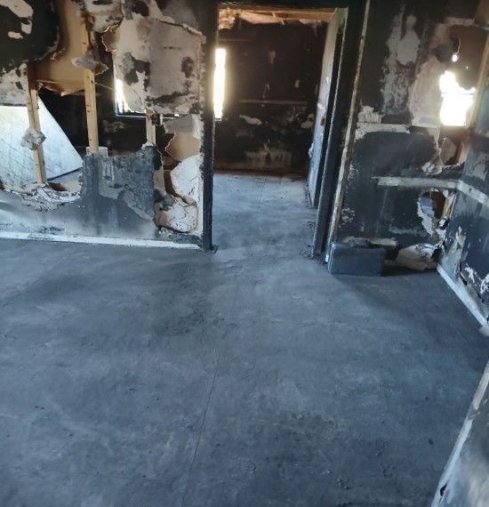 Interior view of a fire-damaged room. Charred walls and flooring, the space is dark and empty.