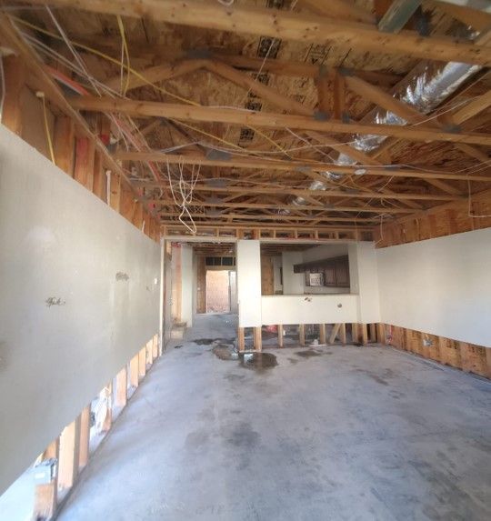 Interior view of a room under renovation, revealing studs, exposed wiring, and partially plastered walls; concrete floor.