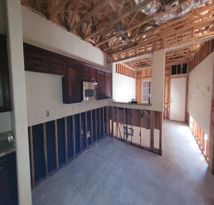 Interior view of a house under construction; exposed studs, partial drywall, and cabinets installed in the kitchen.