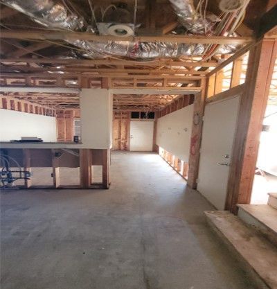Interior of a room under construction, with exposed wooden framing, unfinished walls, and concrete flooring.