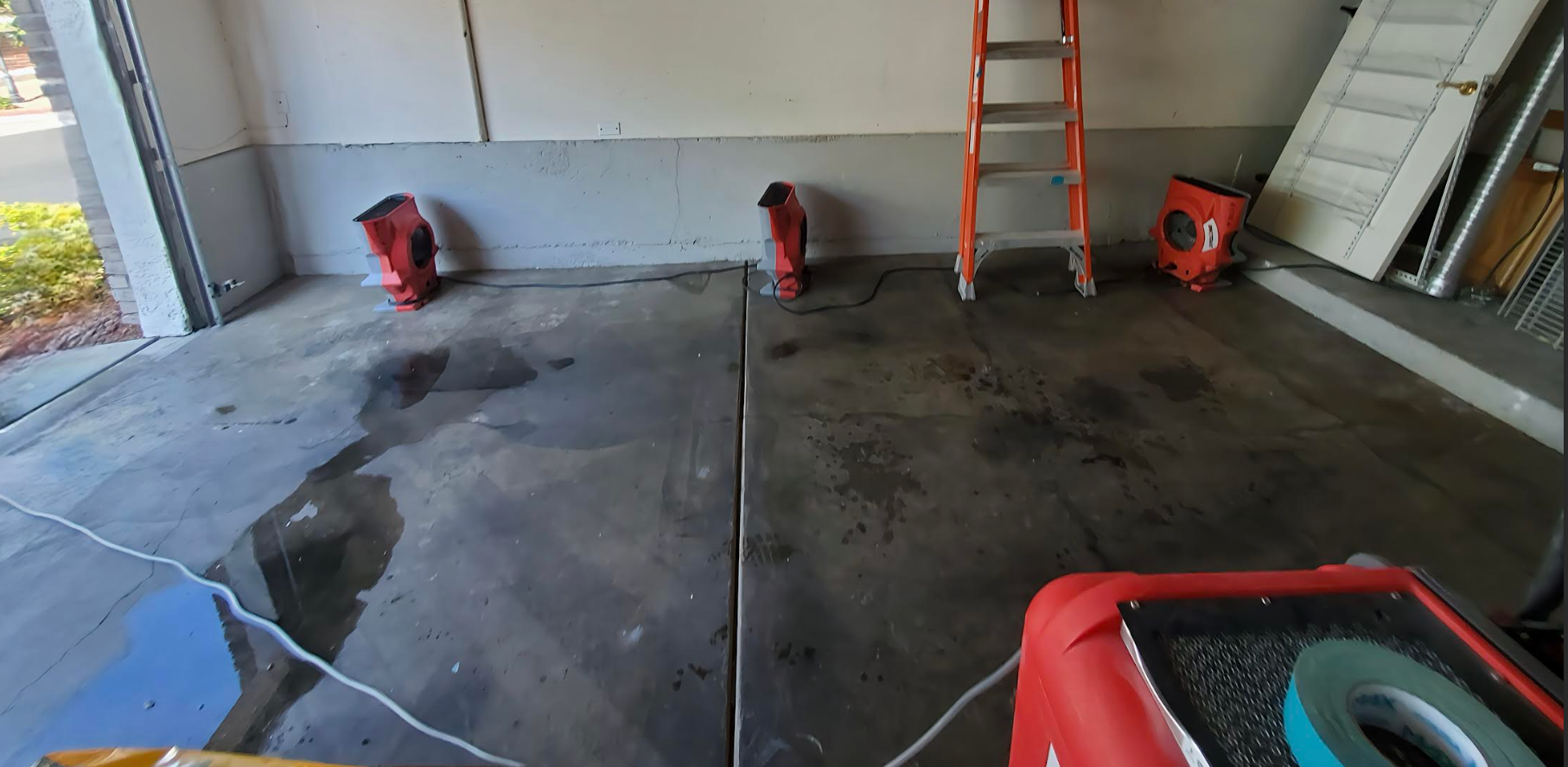 A garage with a ladder, red buckets, and water on the floor, possibly in the process of being worked on.