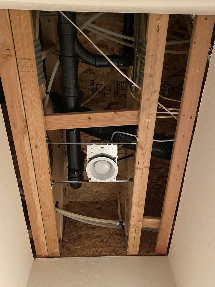 A ceiling with a lot of pipes and wires hanging from it.