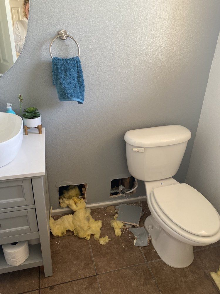 A bathroom with a toilet , sink , and a hole in the wall.
