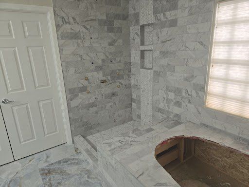 A bathroom with marble tiles , a tub , a shower and a window.