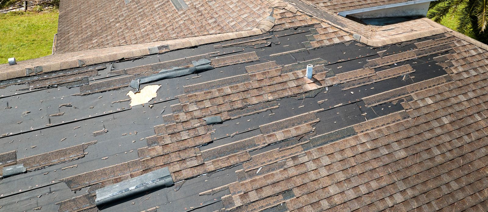 Damaged brown shingle roof with missing shingles, exposing black underlayment; outdoors.