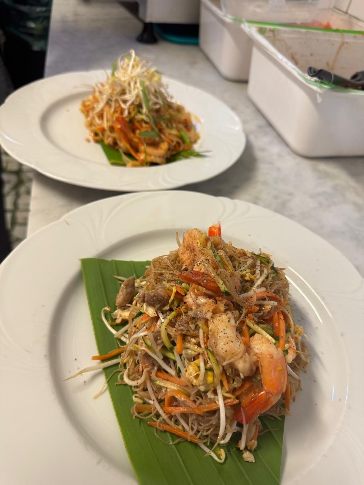 Due piatti di cibo con tagliatelle e gamberi su una foglia verde su un tavolo.