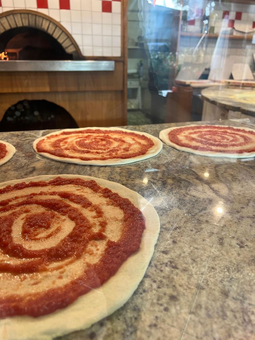 Tre pizze dcon la salsa sopra sul bancone.