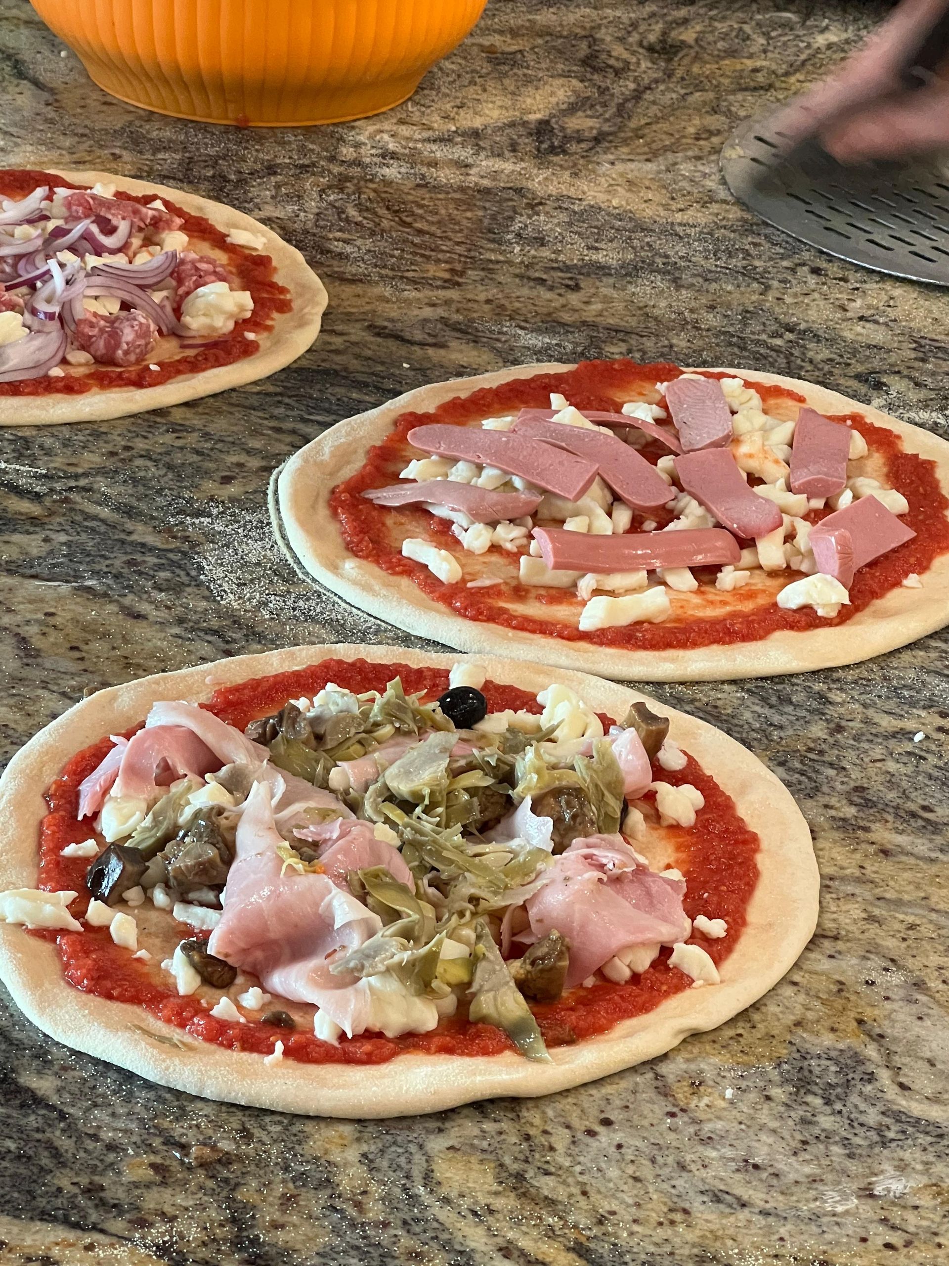 Tre pizze con condimenti diversi sono appoggiate su un bancone.