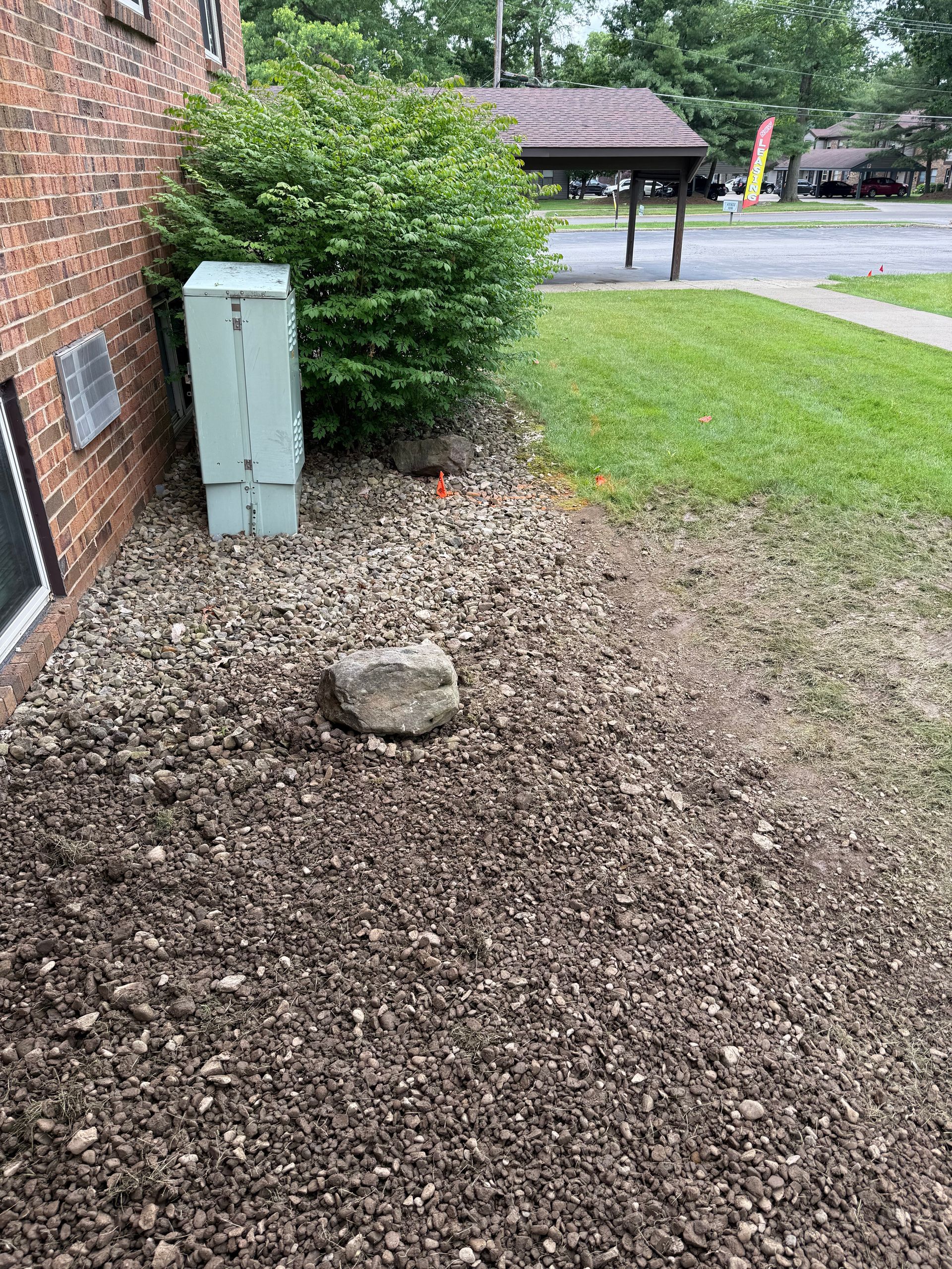 A large rock is sitting in the dirt in front of a brick building.