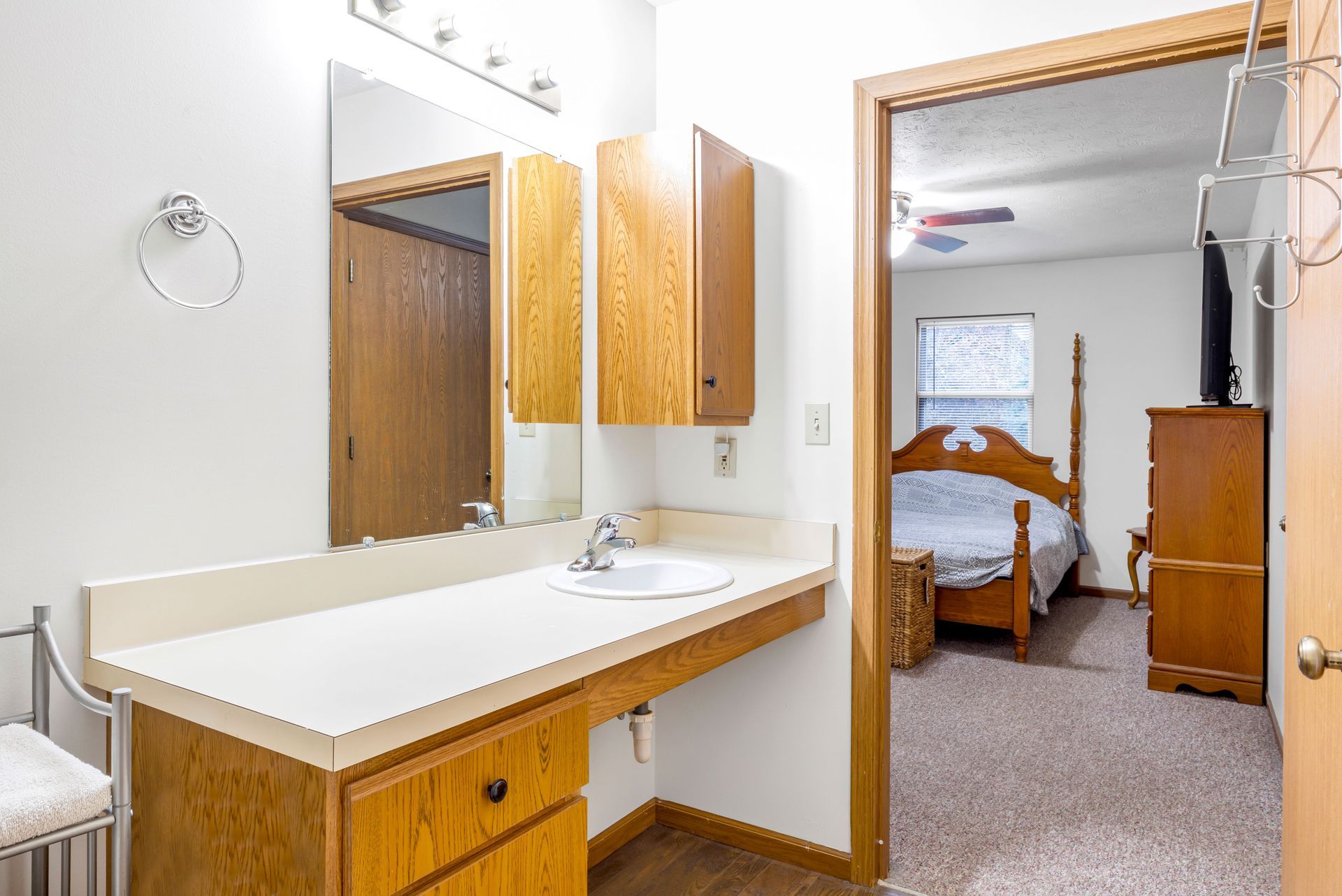 A bathroom with a sink , mirror and dresser next to a bedroom.