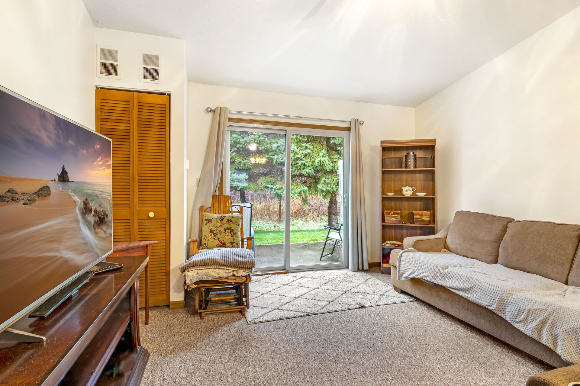 A living room with a couch , chair , television and sliding glass doors.