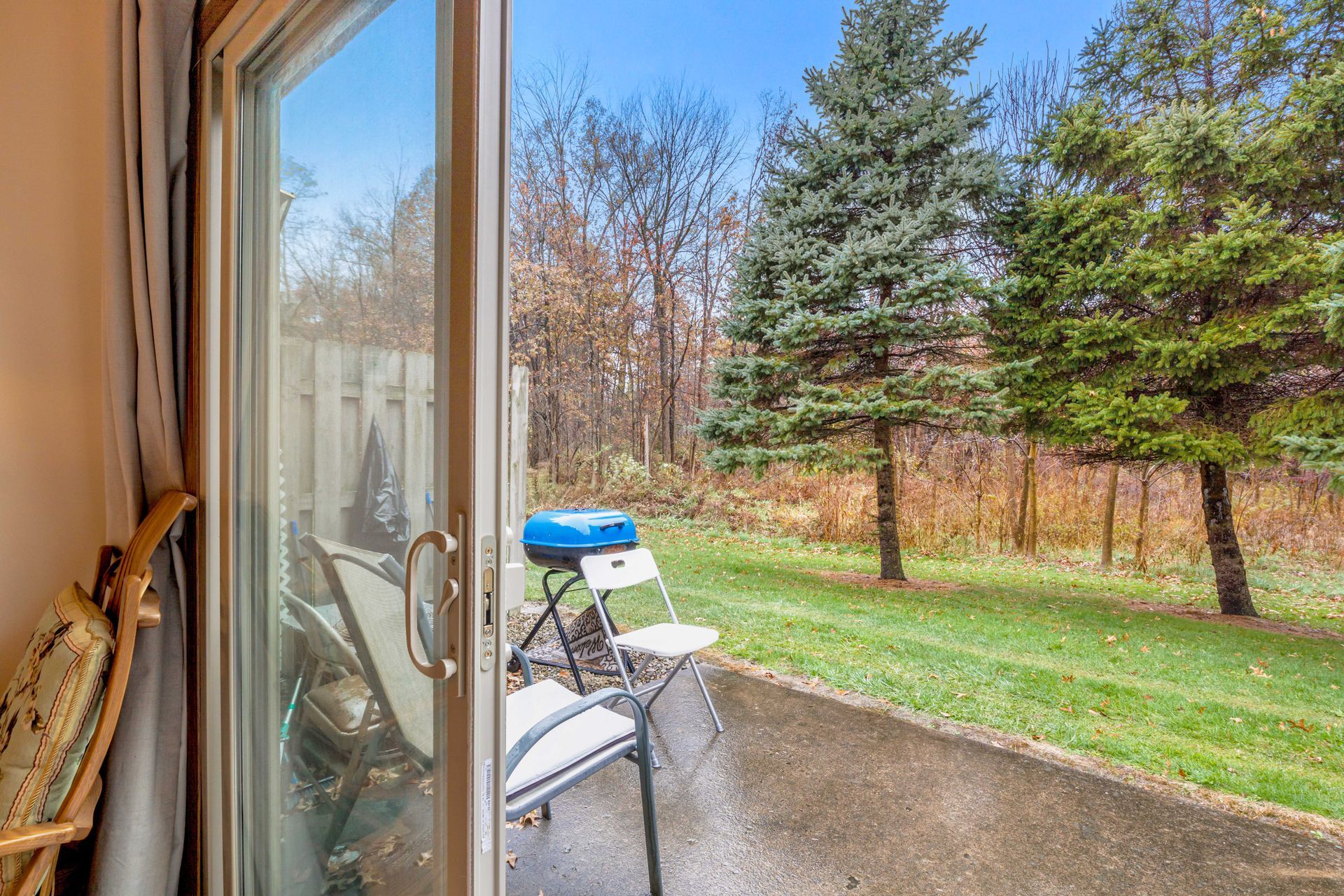 A sliding glass door leading to a patio with a chair and a grill.