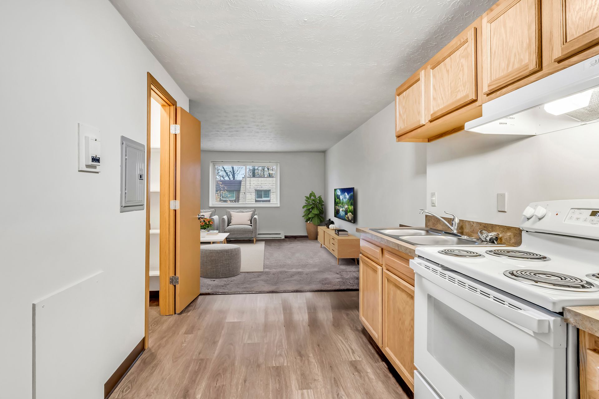 A kitchen with a stove , sink , cabinets and a living room.