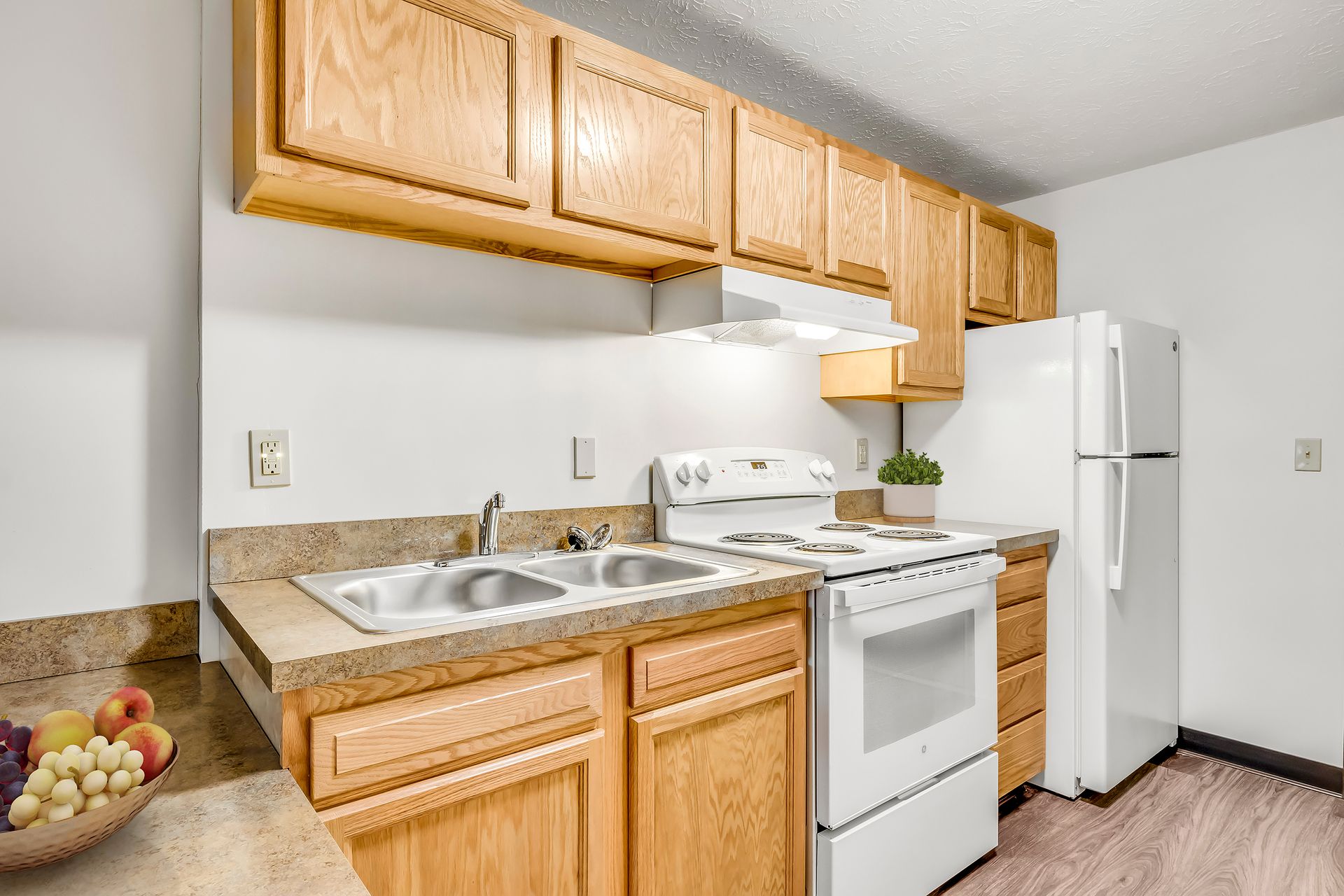 A kitchen with wooden cabinets , a stove , a refrigerator , and a sink.