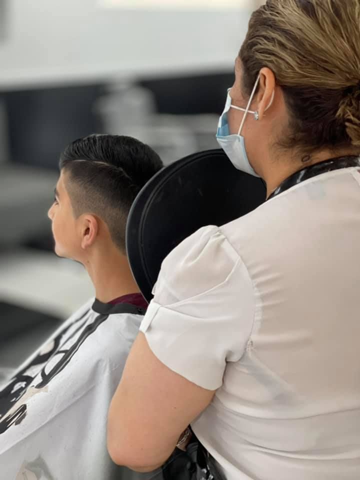 A woman wearing a mask is sitting next to a boy getting his hair cut.