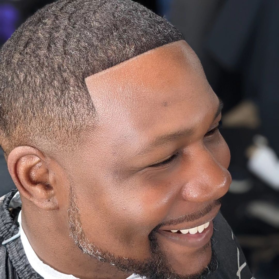 A man with a beard is smiling while getting his hair cut.