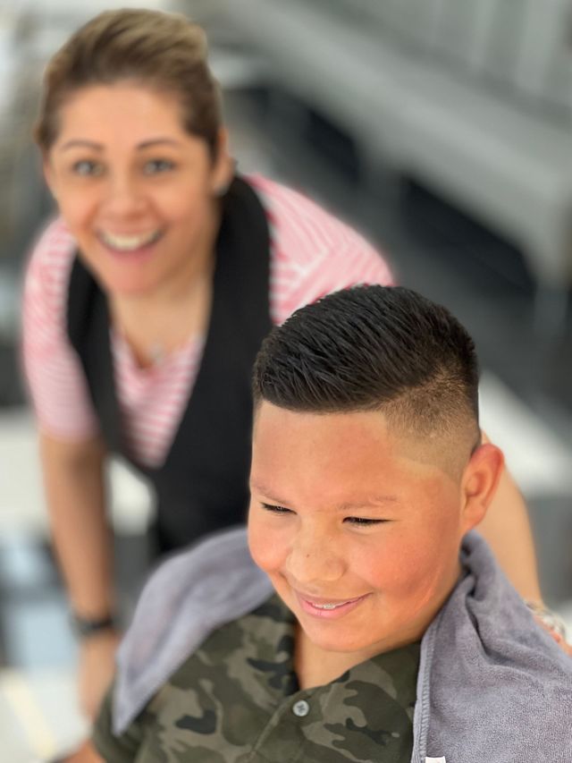 A young boy is getting his hair cut by a woman at a barber shop.