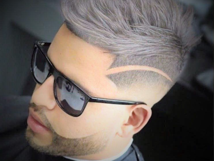 A man with a beard and sunglasses has a shaved line in his hair.