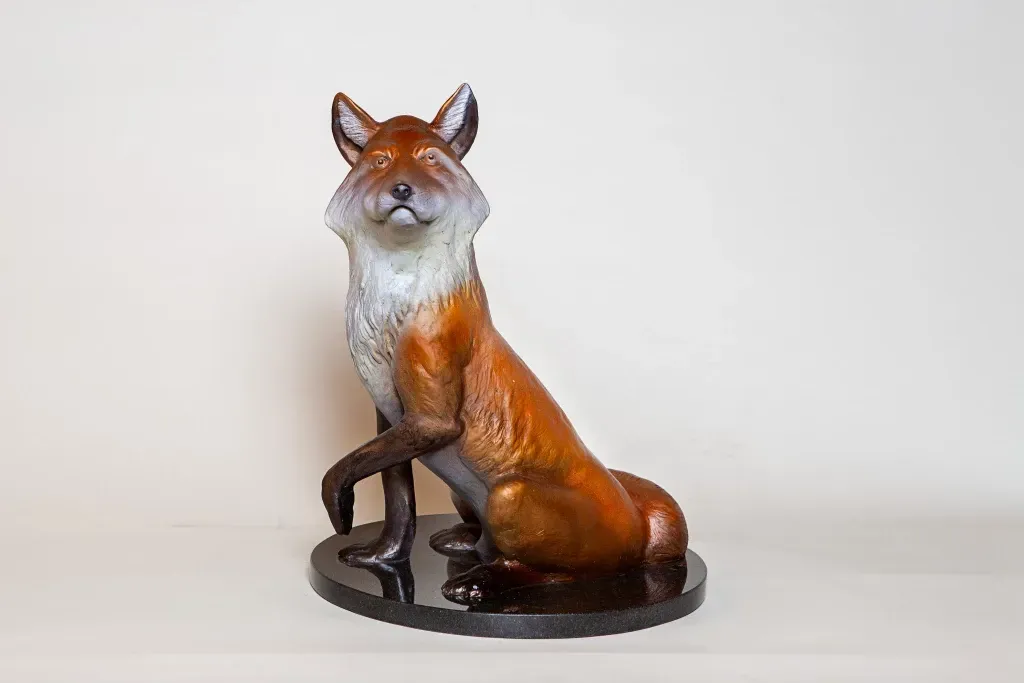 A statue of a fox sitting on a black base.