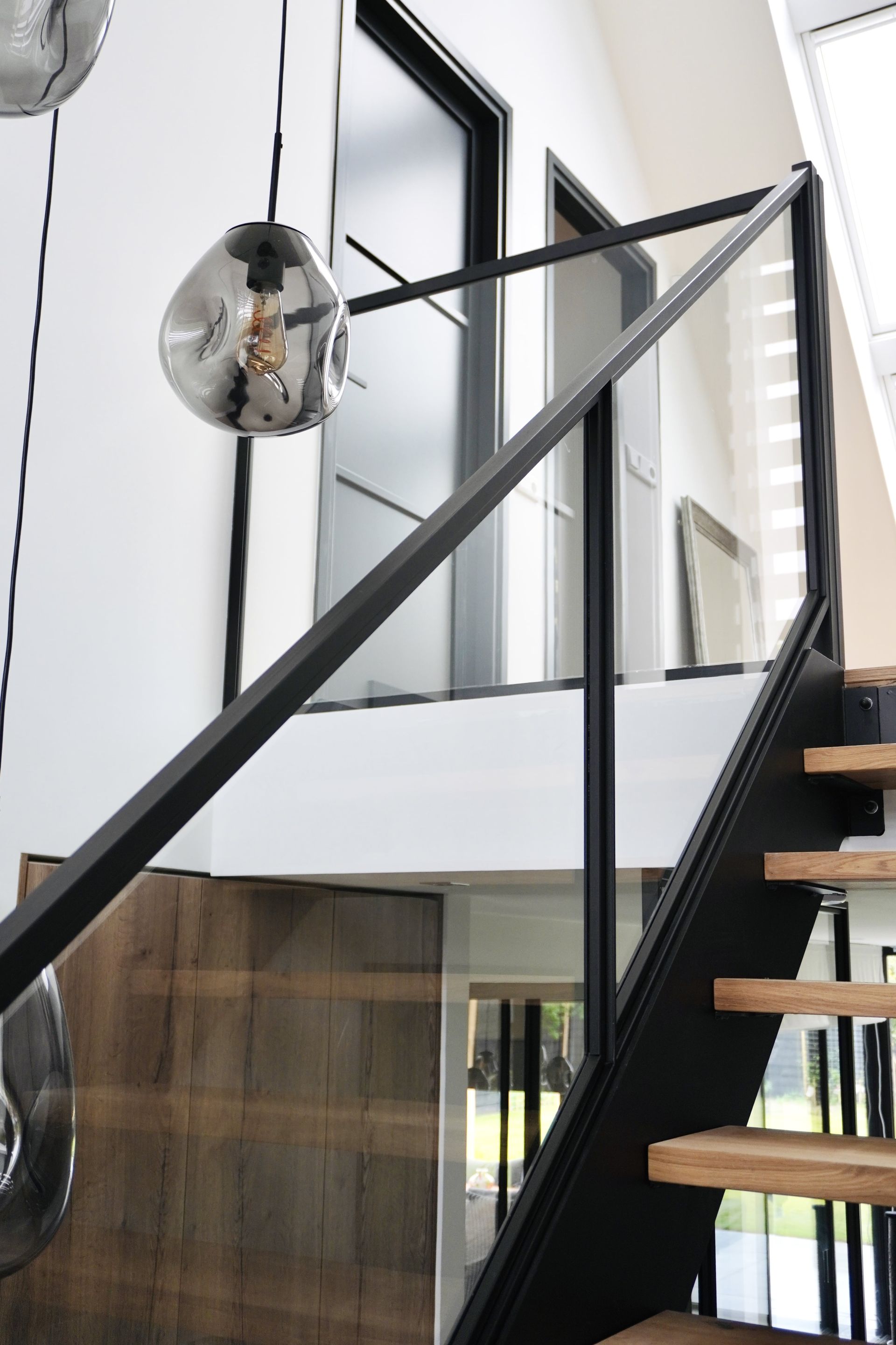 Stalen trap met eikenhouten trede en stalen balustrade met glas