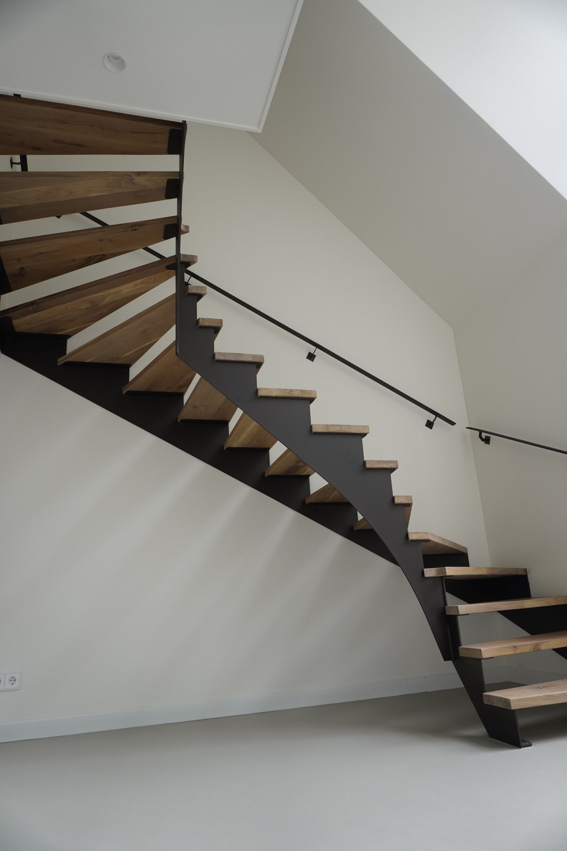 Brons stalen keepboom trap met licht eikenhouten traptreden, voorzien van glazen balustrade