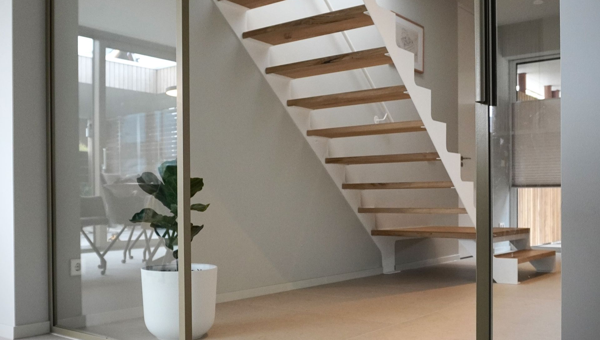 Stalen witte keepboom trap met witte leuning en bruine treden. Brons stalen schuifdeuren met glas.