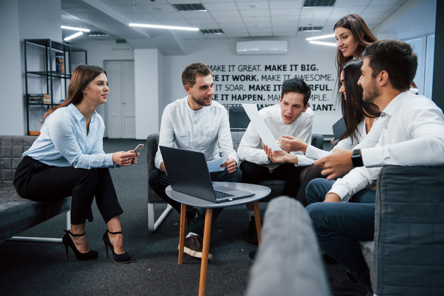 A diverse professional team in business attire meets in a modern office, sitting together and discussing documents.