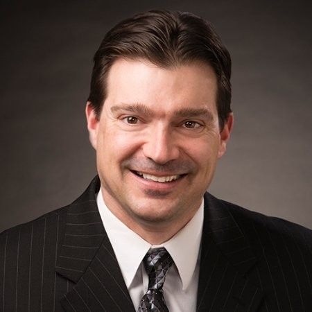 A smiling professional in a pinstriped suit and tie posing for a portrait against a gray background.