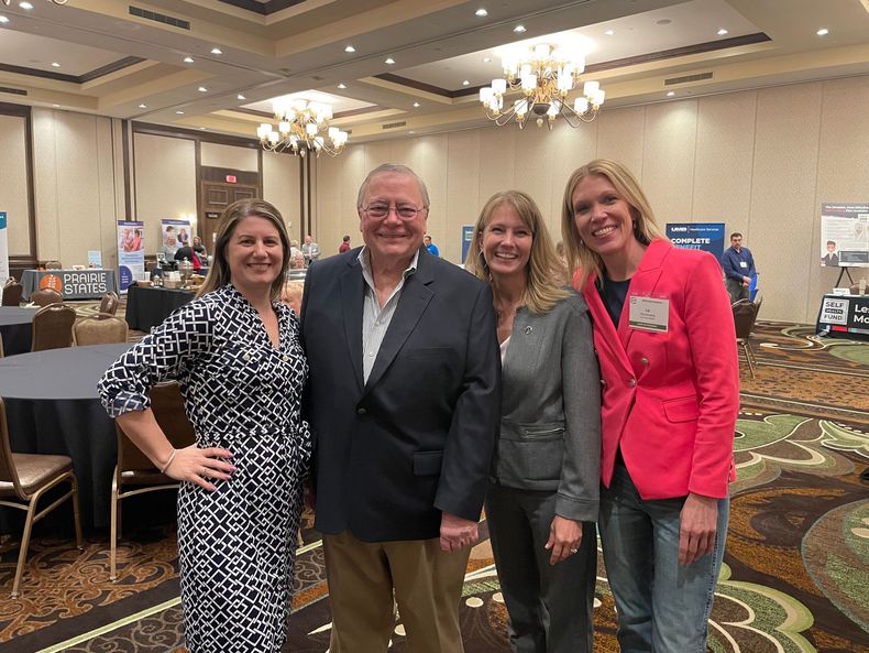 A group of three people in a bright office sit at a table, discussing documents and smiling during a professional meeting.