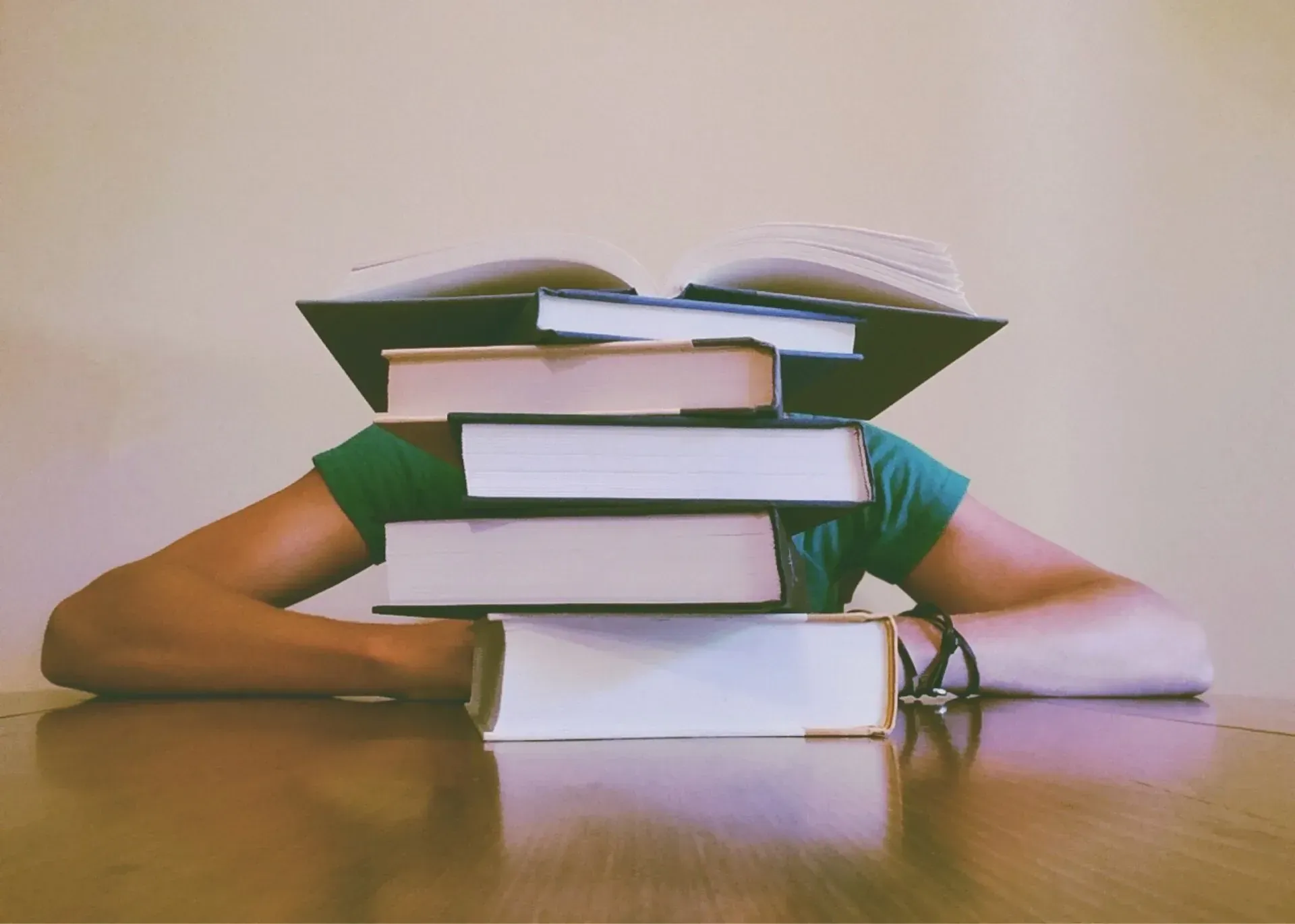 A person wearing a green shirt rests their chin on a stack of books, obscuring their face.
